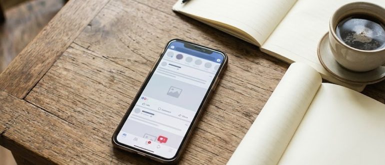 Смартфон с лентой соцсети, блокнот и монеты на рабочем столе